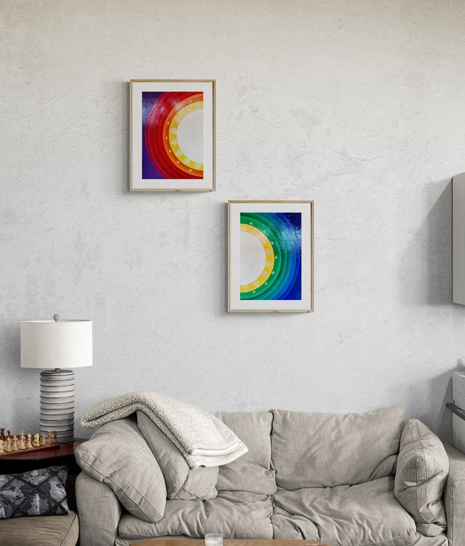 Two framed paintings on top of a sofa representing a Sun Mandala in half with feminine colors one and masculine colors the other.